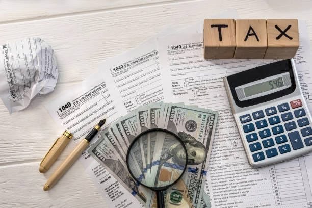 Calculator, magnifying glass over dollar bills, and tax forms with the word TAX, representing planning and adjustments for taxes in the US.